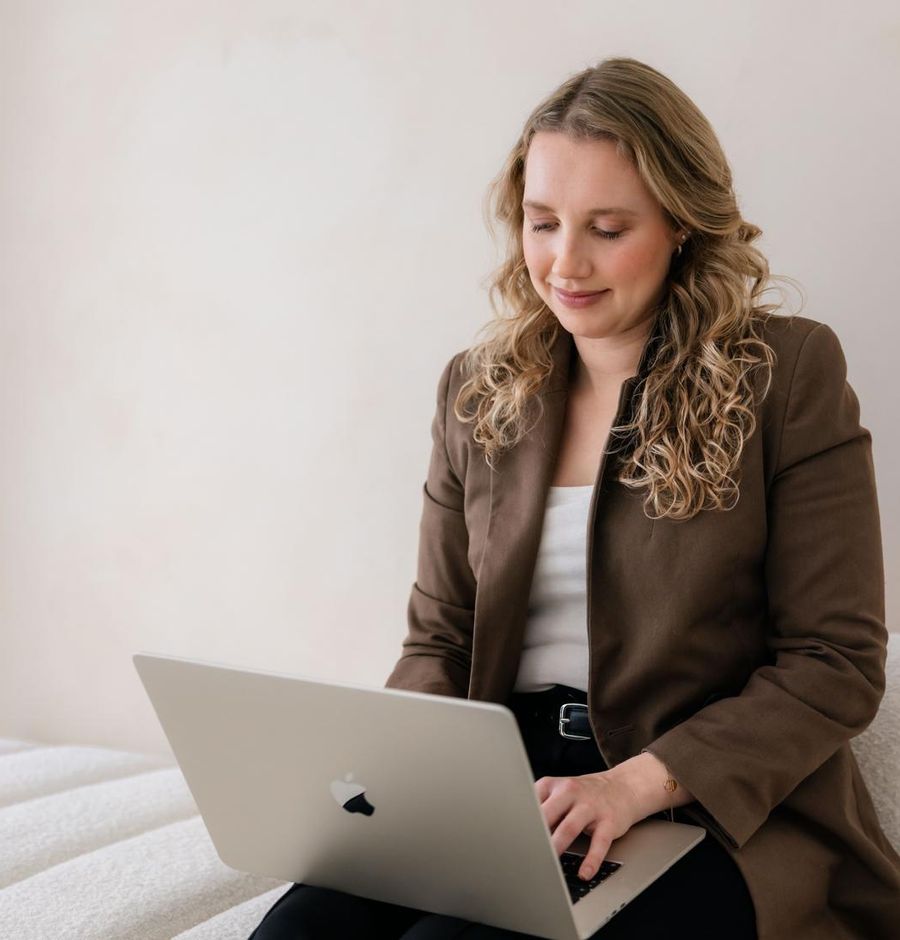 Debra Bekker werkt op haar laptop op een witte bank